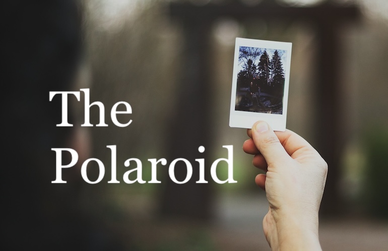 Image of a hand holding a polaroid photo, which depicts a family standing together outside
